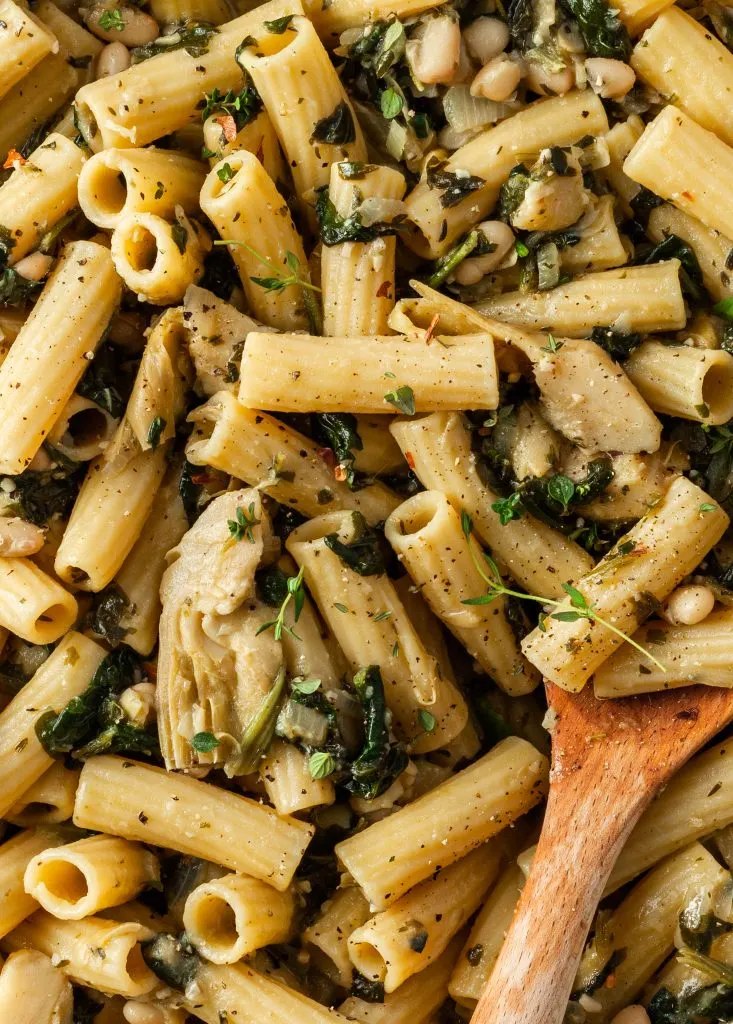 Close up of the spinach artichoke pasta in the pot being stirred with a wooden spoon. 