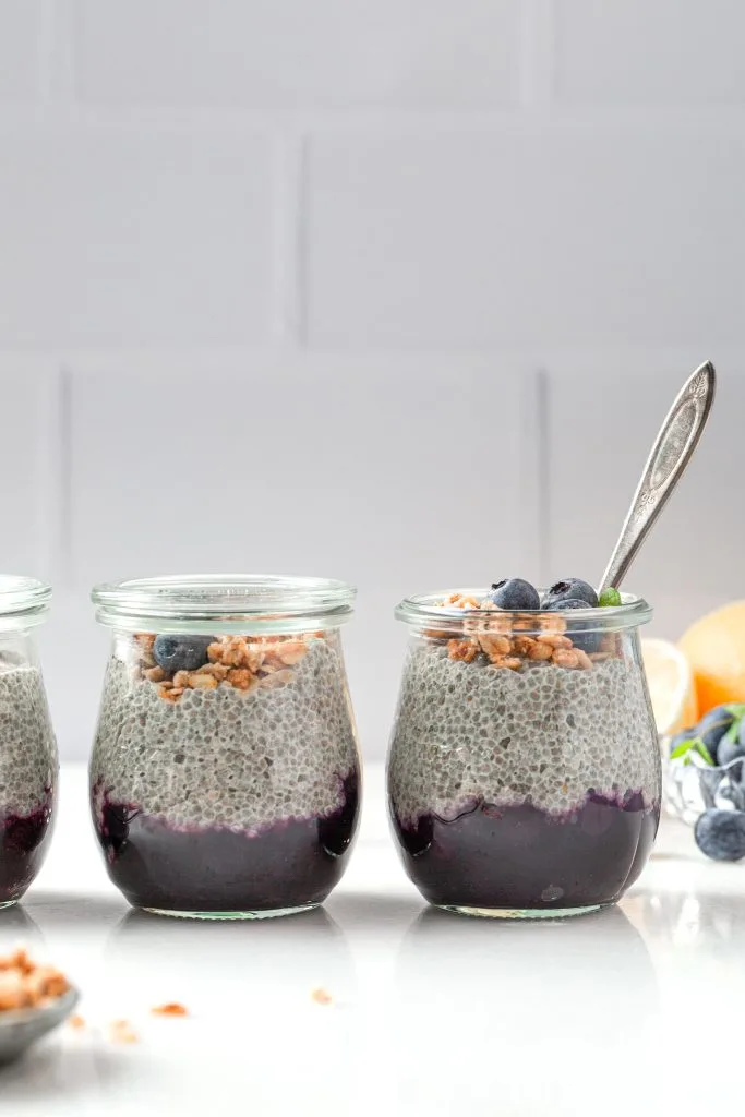 Three jars of lemon chia seed pudding on a white kitchen counter, 2 with lids showing the meal prep and one ready to go with a spoon in it. 