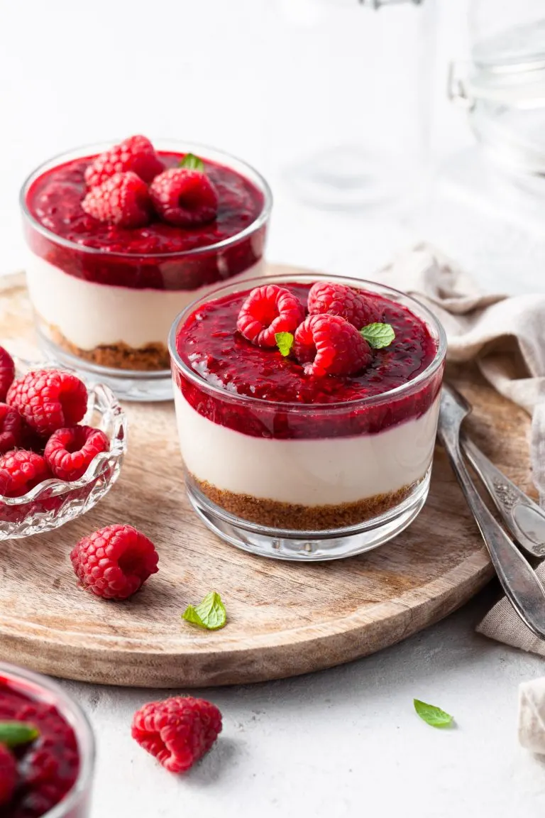 No Bake Vegan Cheesecake Jars garnished with raspberries, served on a wooden tray