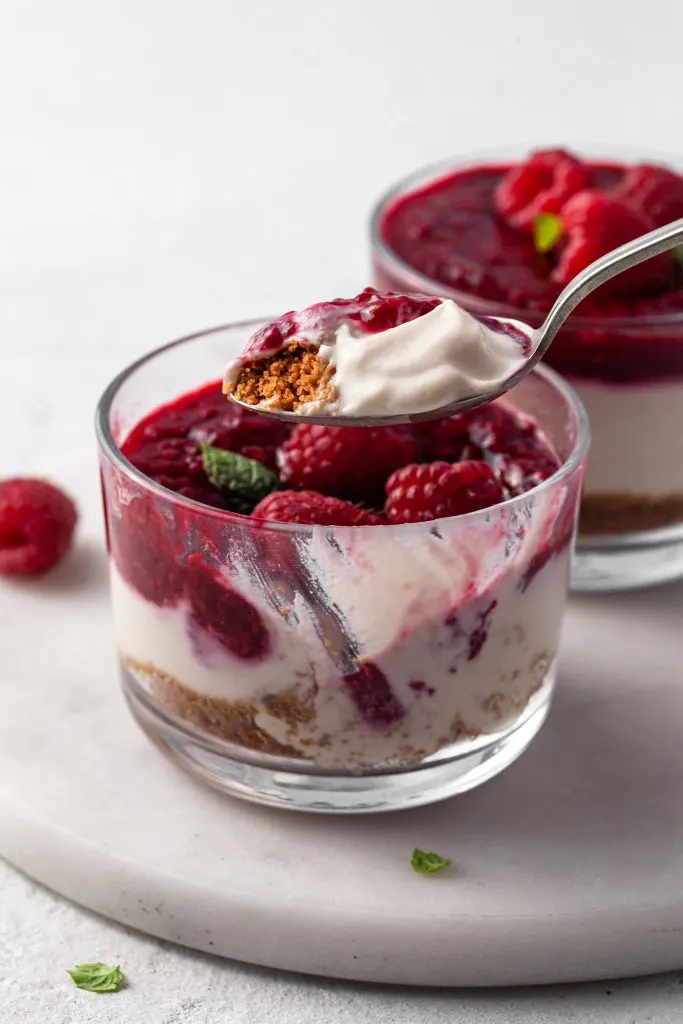 A spoonful of dairy free no bake cheesecake above a single serve cheesecake demonstrating the creamy texture of the vegan filling. 