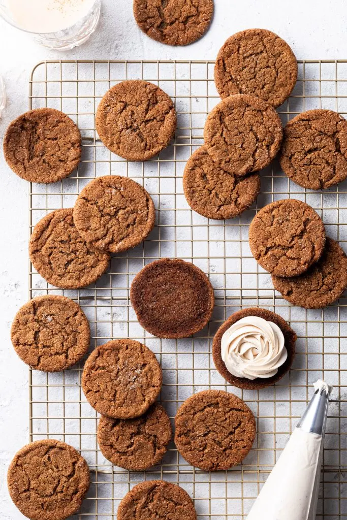 Molasses cookies on a cooling rack, a piping bag of frosting and one cookie topped with a rose shaped dollop of piped frosting