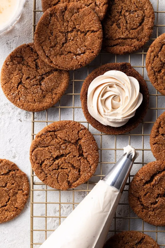 A close up of the bottom of a molasses cookie covered in eggnog frosting on a cooling rack with other molasses cookies