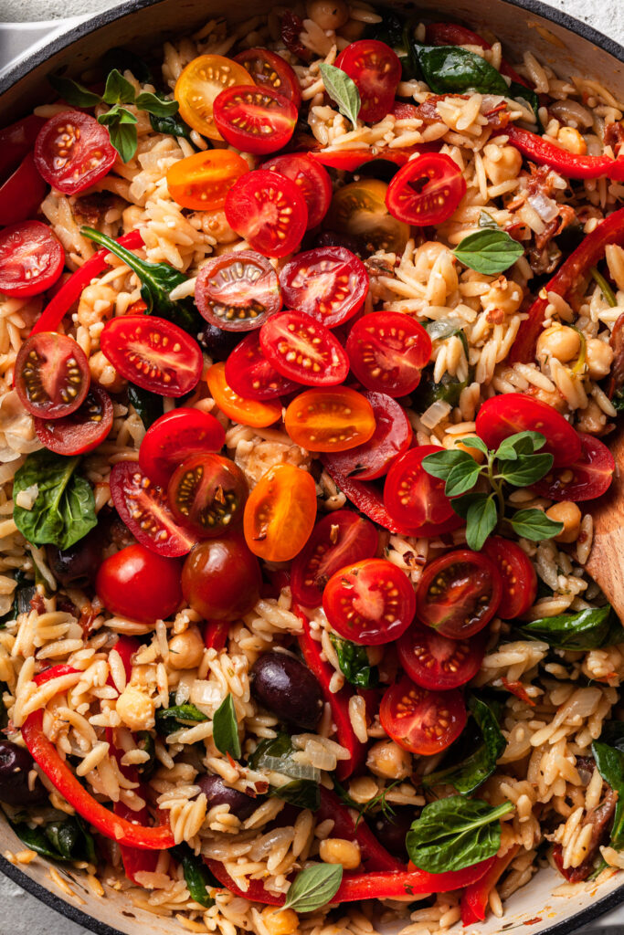 Close up of the prepared Greek orzo and garbanzo beans, topped with sliced cherry tomatoes and fresh herbs.  