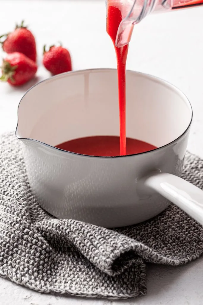 Strawberry being poured from a blender into a small white pot. 