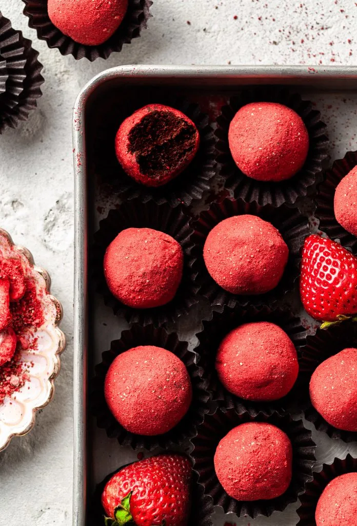 A box of homemade vegan chocolate strawberry truffles, with a couple of fresh strawberries tucked in.