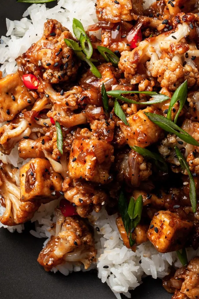 A close up of tofu and cauliflower in a brown sauce over white rice. 