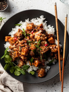 Flat lay of a black bowl filled with tofu and cauliflower in a vegan black pepper sauce.