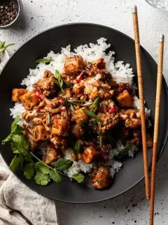 Flat lay of a black bowl filled with tofu and cauliflower in a vegan black pepper sauce.