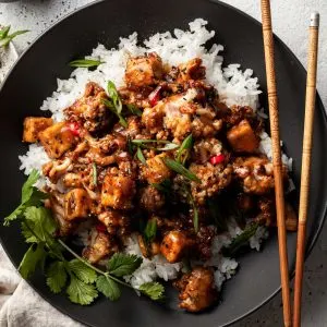 Flat lay of a black bowl filled with tofu and cauliflower in a vegan black pepper sauce.