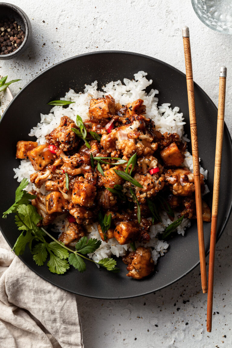Flat lay of a black bowl filled with tofu and cauliflower in a vegan black pepper sauce.