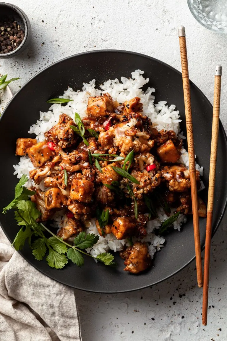 Flat lay of a black bowl filled with tofu and cauliflower in a vegan black pepper sauce.