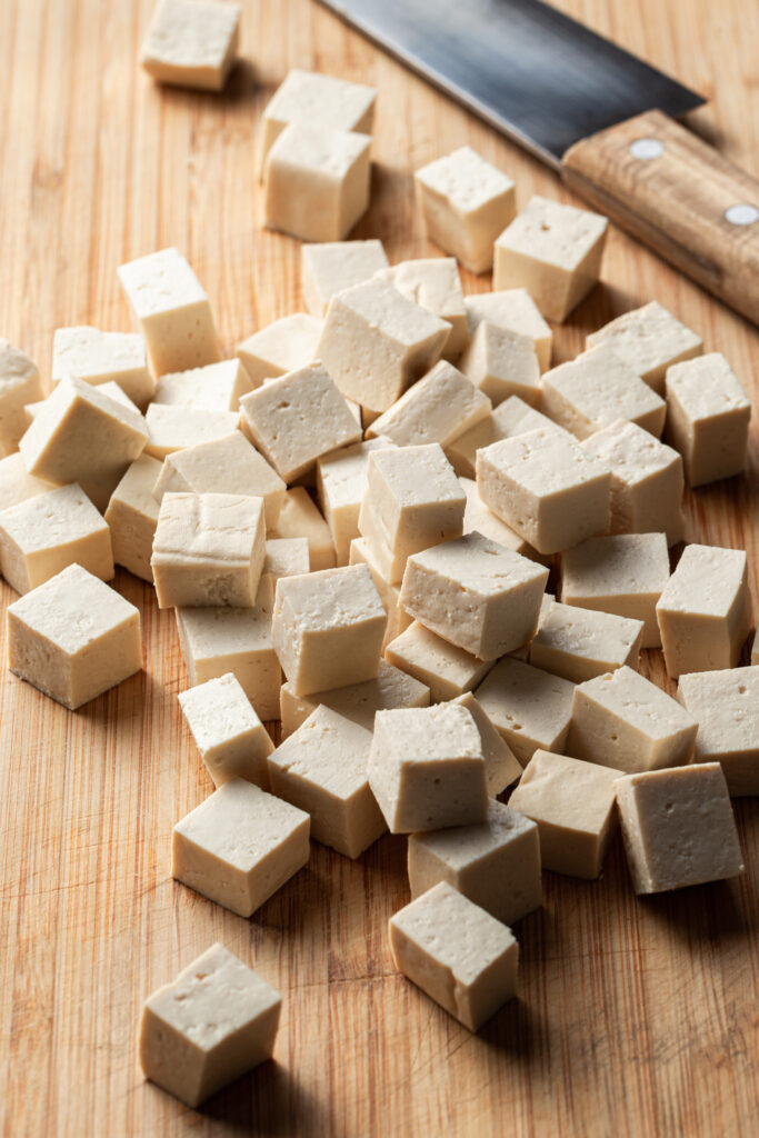 Freshly cubed tofu on a cutting board beside a chef's knife. 