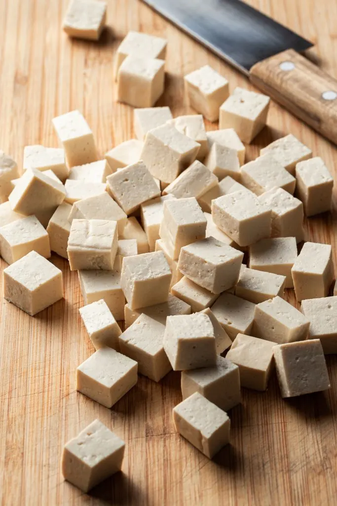 Freshly cubed tofu on a cutting board beside a chef's knife. 