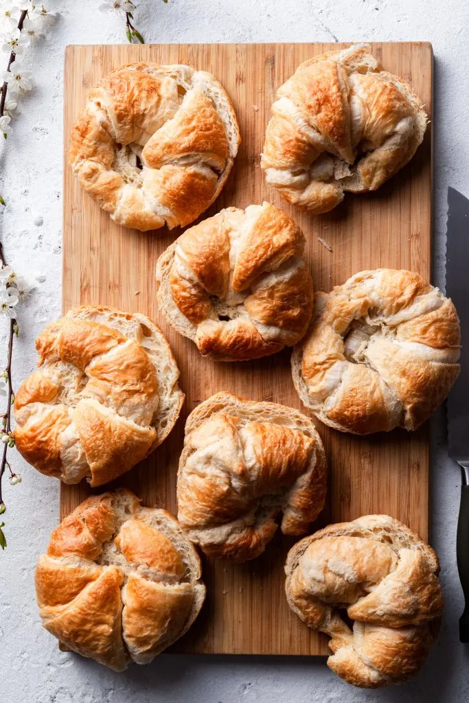 A bamboo cutting board topped with 8 plain croissants which have been sliced in half. 
