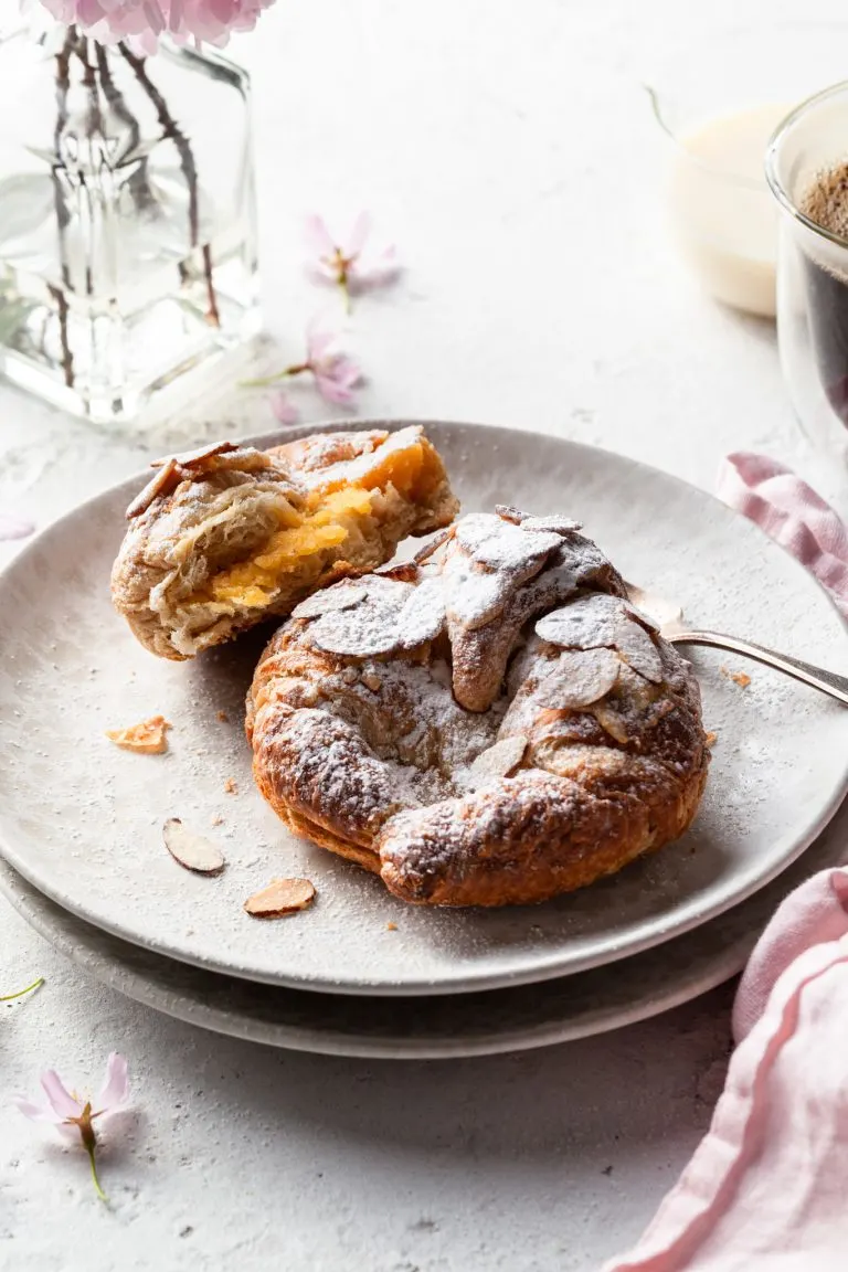 Two almond croissants on a cream plate, one is broken open to reveal the creamy filling.