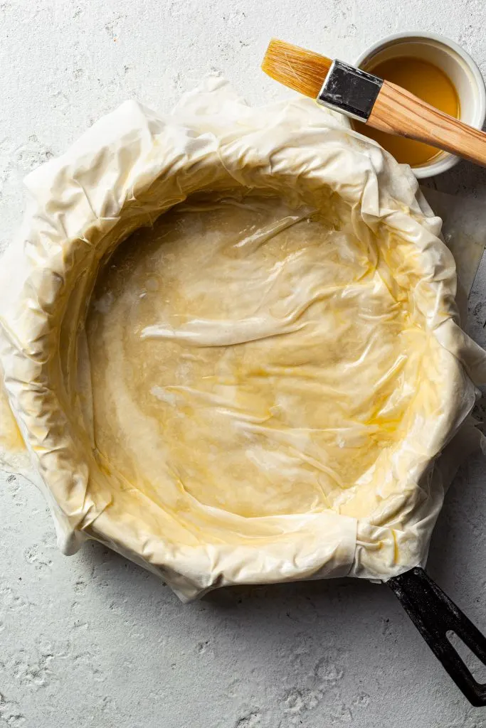 Cast iron skillet lined with layers of phyllo pastry dough, brushed with oil.