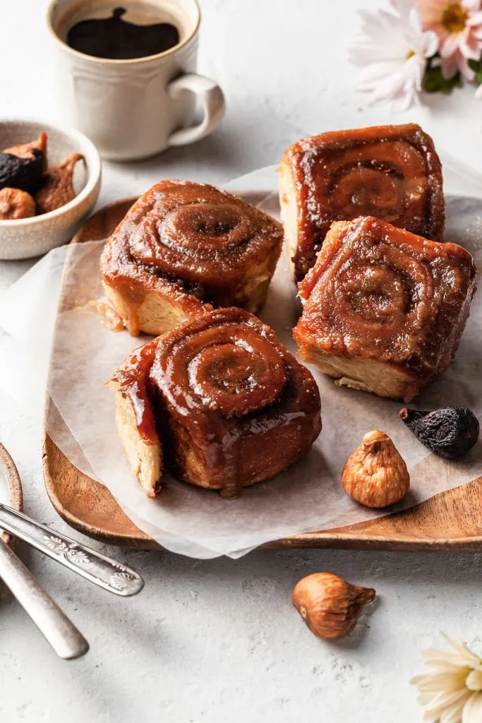 Four sticky buns on a paper lined wooden plate. 