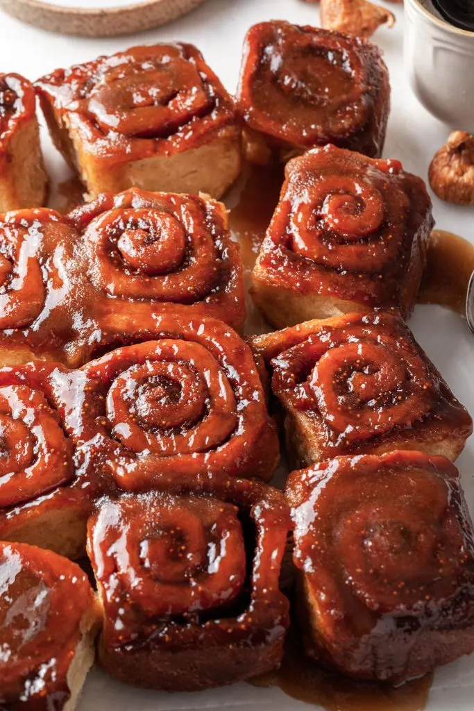 Side view of a dozen fig sticky buns on a white marble slab. 