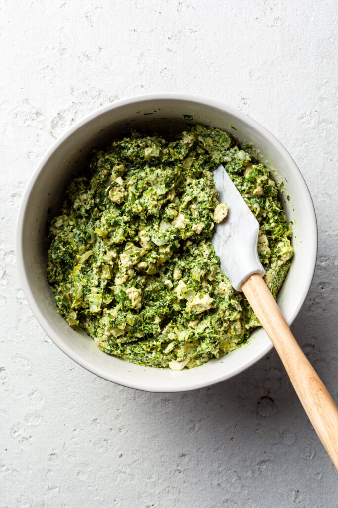 A white bowl filled with spinach filling for the spanakopita. 