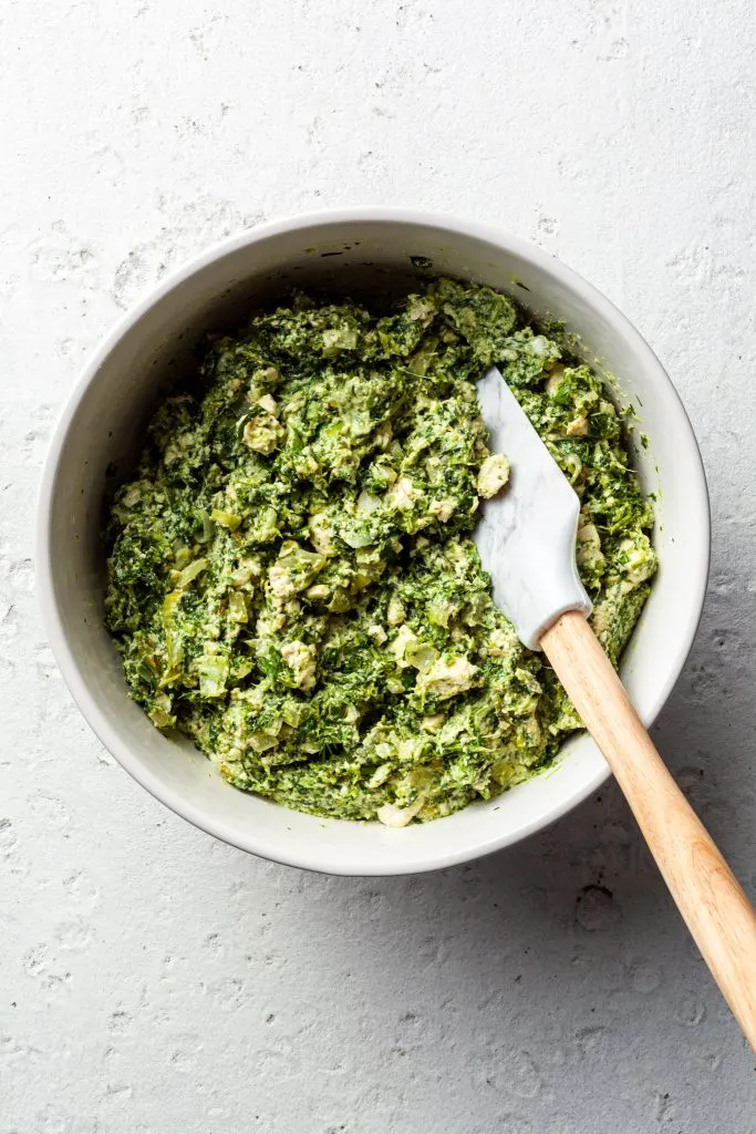 A white bowl filled with spinach filling for the spanakopita. 
