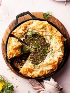 A cast-iron pan filled with a spanakopita, with 2 slices cut and one missing.