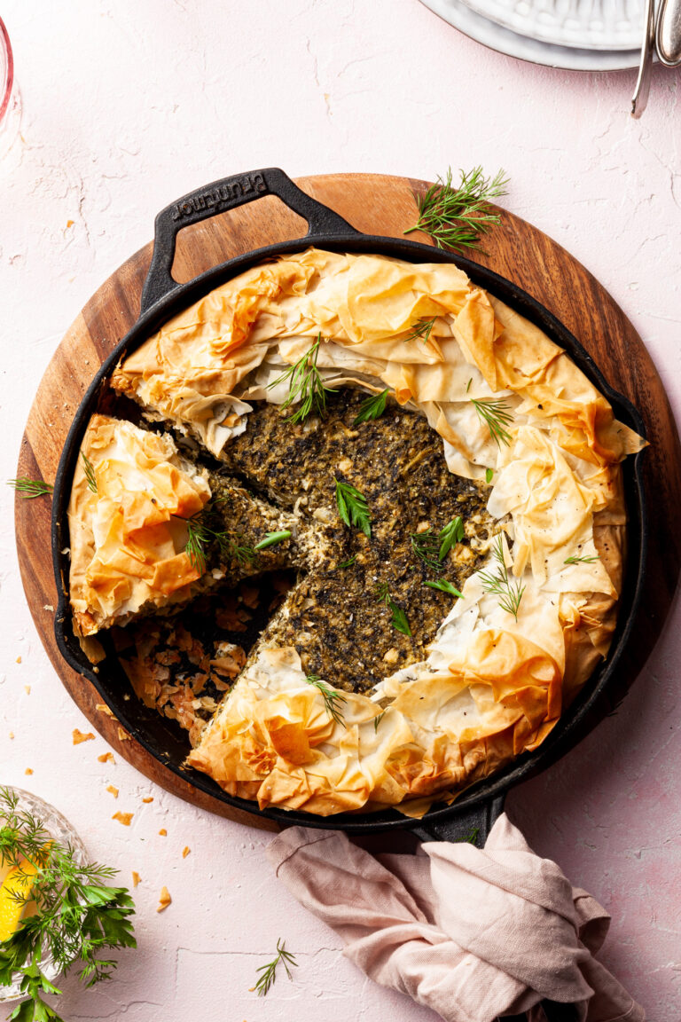 A cast-iron pan filled with a spanakopita, with 2 slices cut and one missing.
