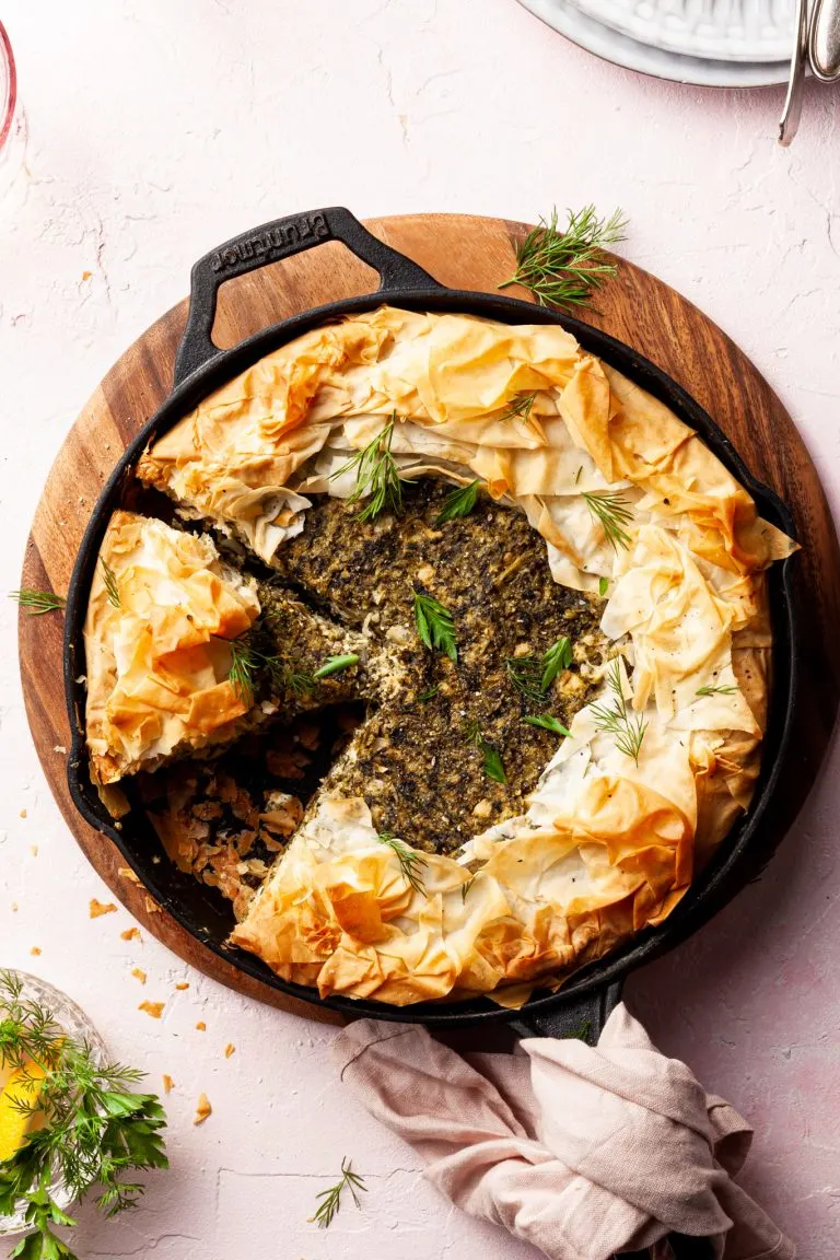 A cast-iron pan filled with a spanakopita, with 2 slices cut and one missing.