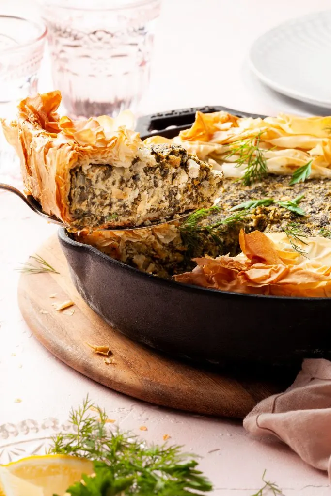 A slice of spinach pie being served from a black skillet. 