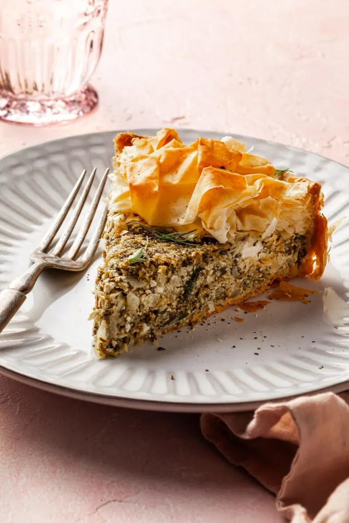 A pie shaped slice of spanakopita on a white plate. 