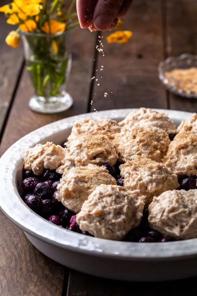 Coarse sugar being sprinkled onto the tops of the biscuits on over frozen blueberries.