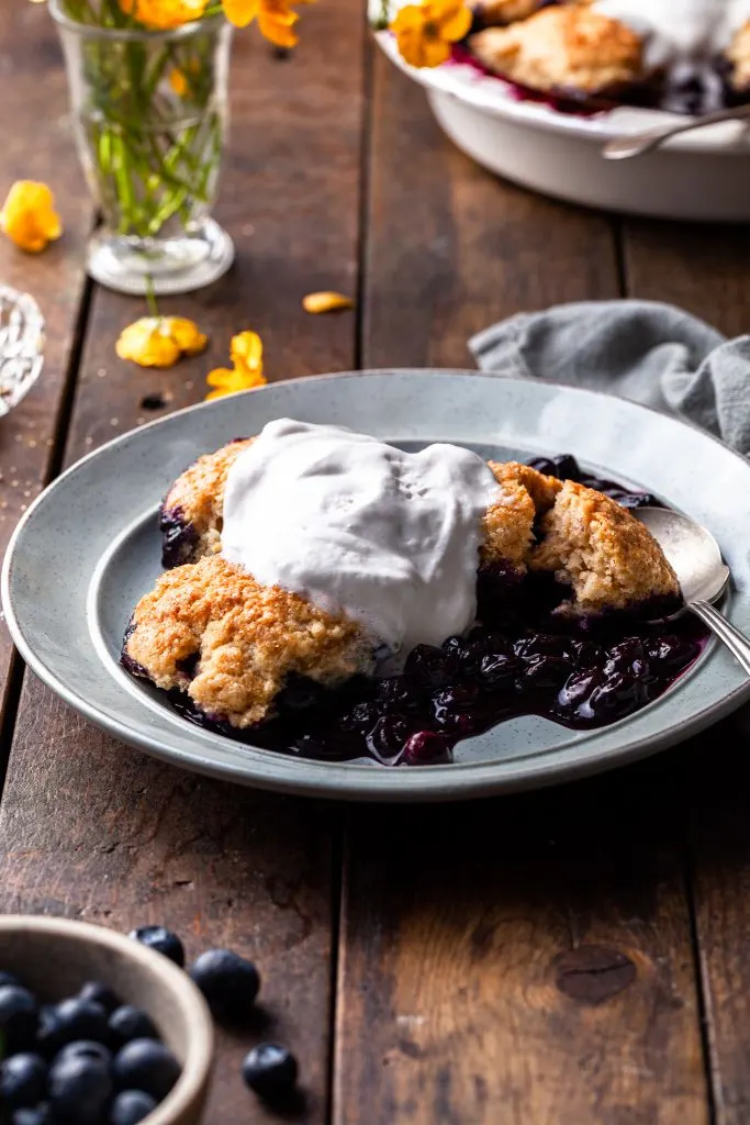 A serving of berry dessert on a light blue plate topped with melting whip.