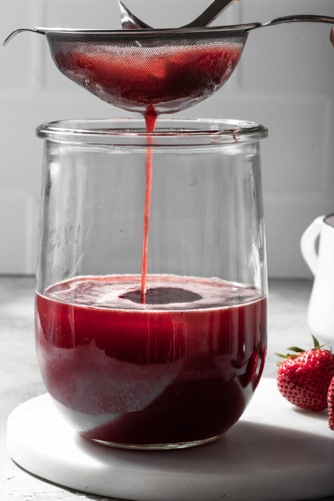 Fruit shrub being strained into a glass canister.