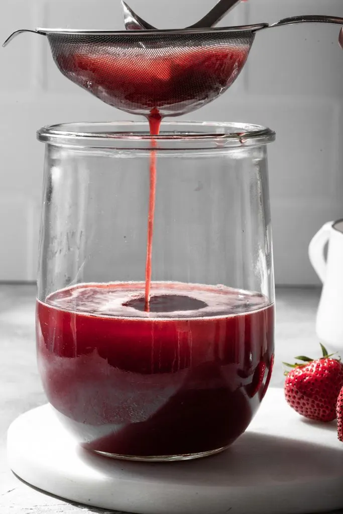 Fruit shrub being strained into a glass canister.