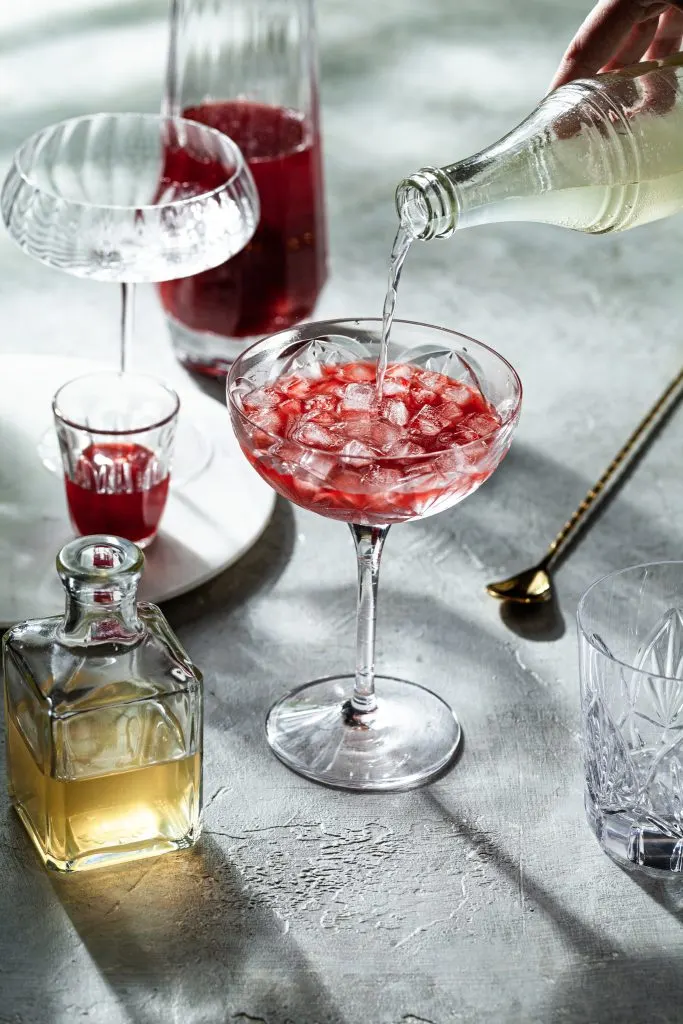 Ginger beer being poured into a glass filled with ice and shrub syrup.