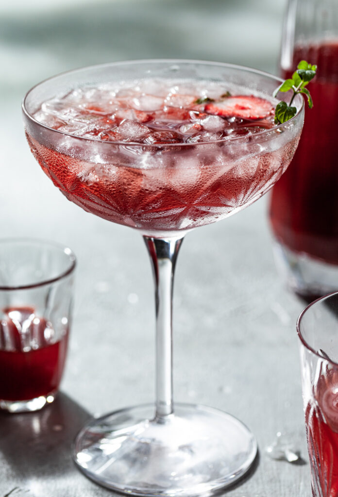 Side view of a coup stem glass covered in condensation, filled with crushed ice and a red drink. 