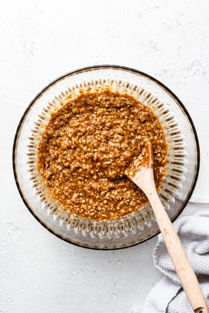 A glass bowl full of oatmeal cookie batter and a wooden spoon. 