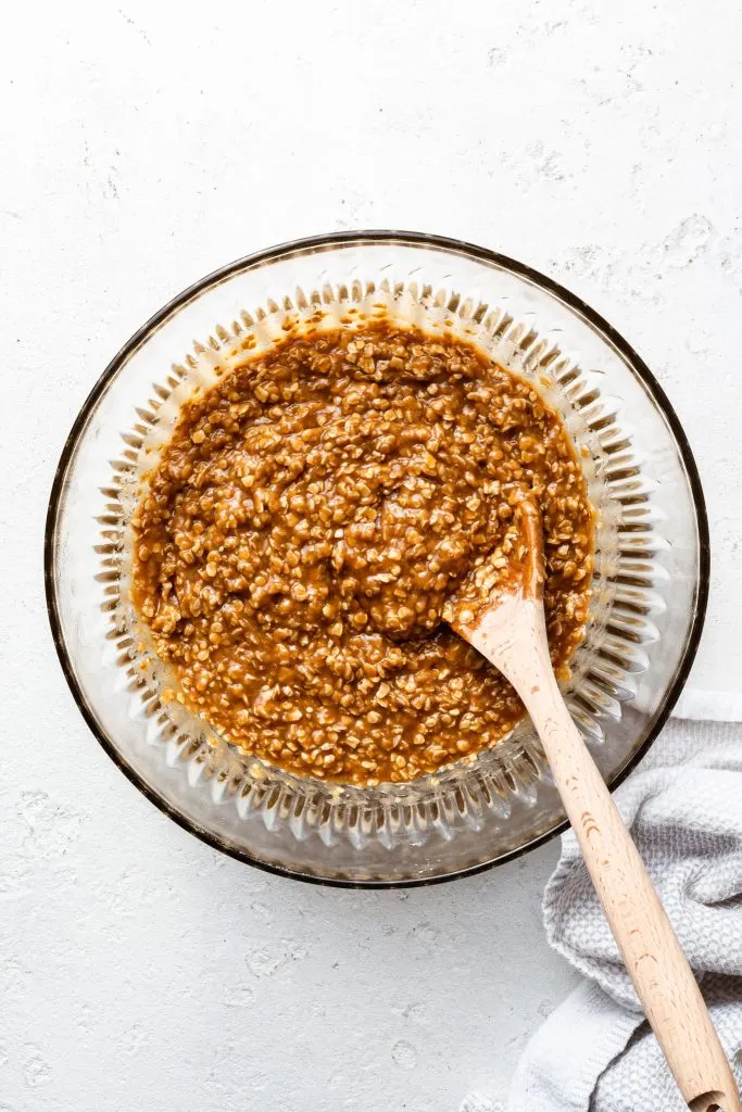 A glass bowl full of oatmeal cookie batter and a wooden spoon. 
