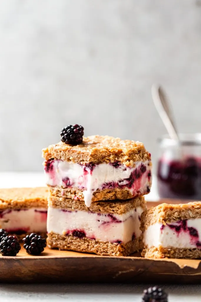 A wooden platter containing 4 ice cream sandwiches, garnished with blackberries. 