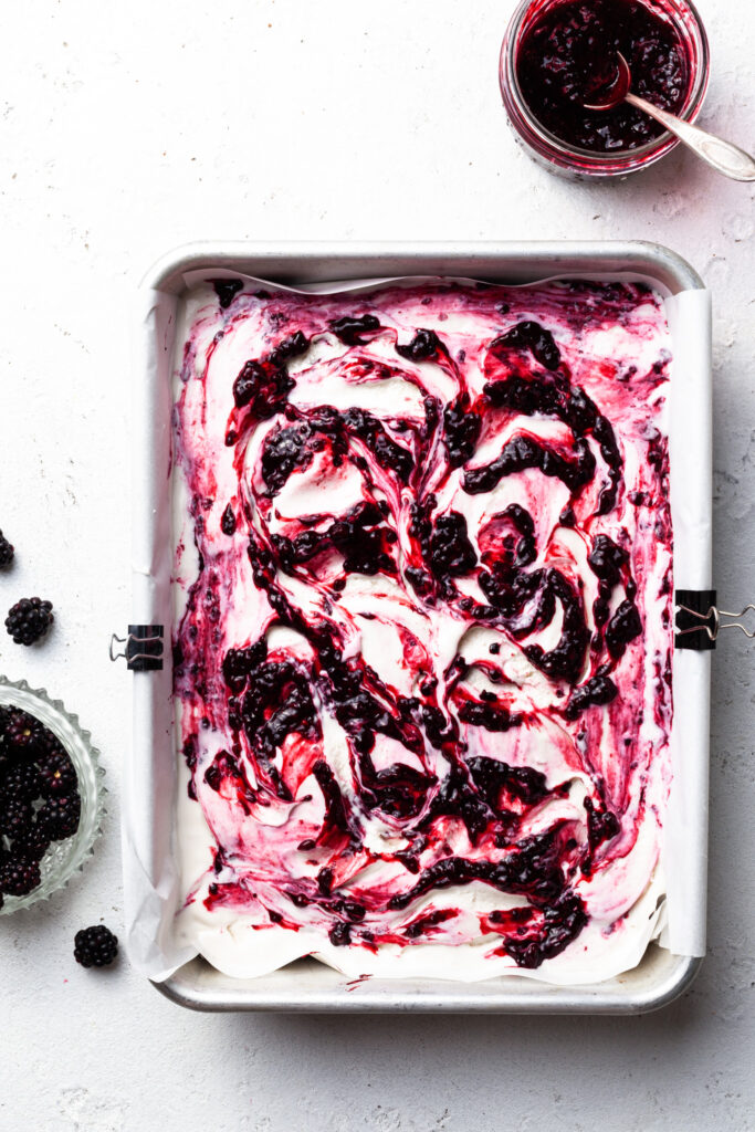 Swirls of berries through white ice cream in a parchment lined baking tin. 