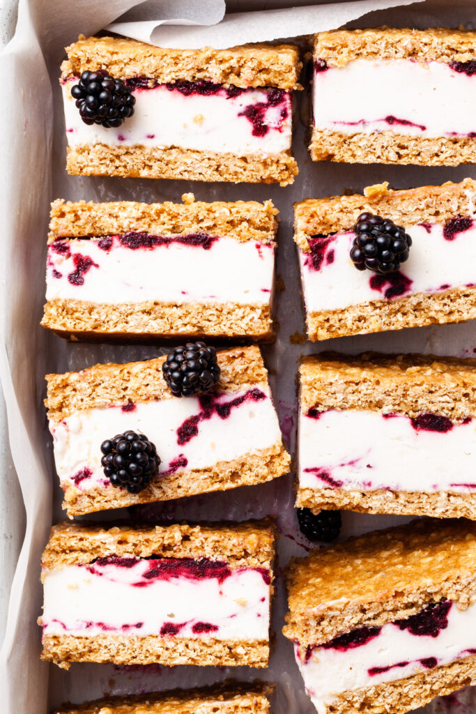 A close up shot of ice cream sandwiches on their sides, with scattered fresh blackberries. 