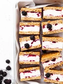 Baking tin lined with white parchment, filled with ice cream sandwiches that contain and purple swirl through the white ice cream layer.
