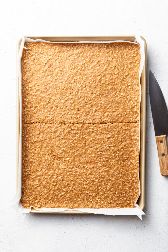 A half sheet baking pan lined with parchment paper and filled with a baked cookie slab cut in half 