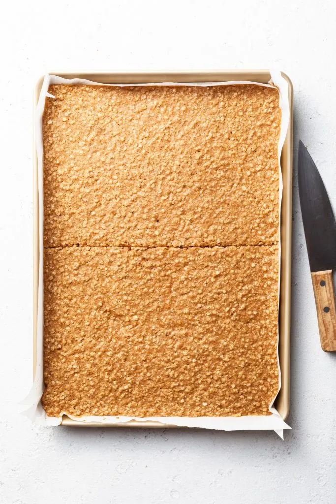 A half sheet baking pan lined with parchment paper and filled with a baked cookie slab cut in half 