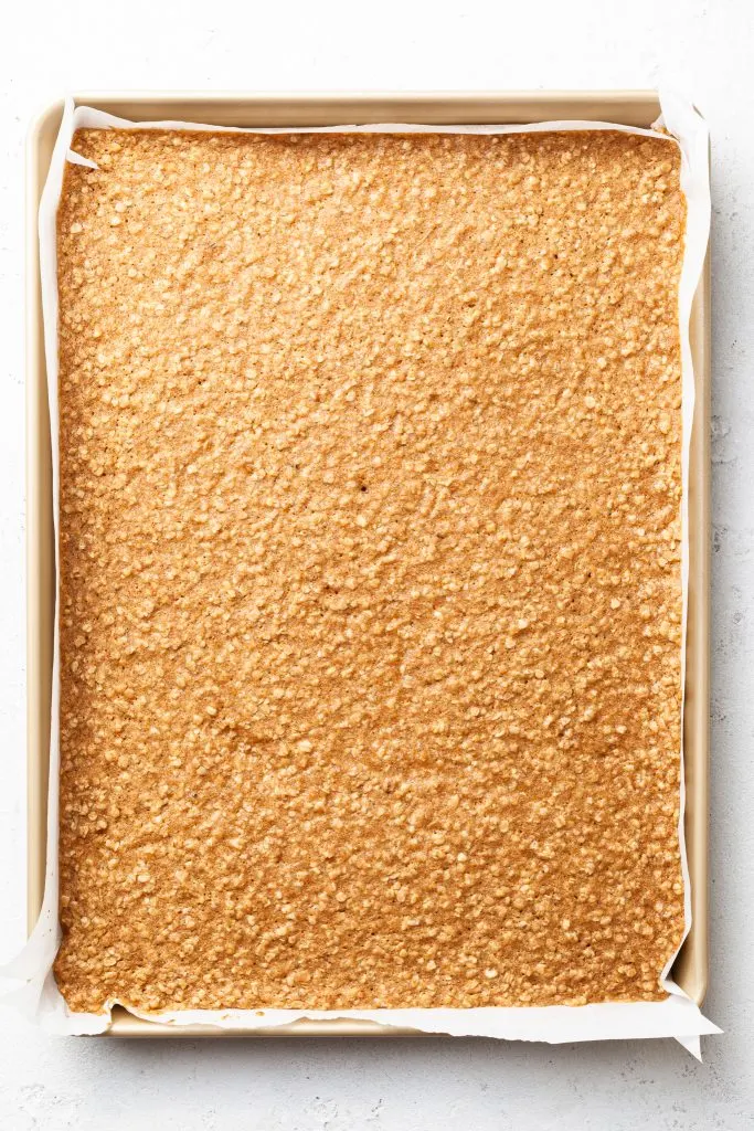 A half sheet baking pan lined with parchment paper and filled with a baked cookie slab.