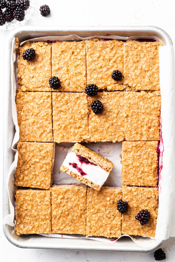 A rectangular metal pan filled with sliced ice cream bars - one is lying on its side revealing the vanilla ice cream and berry swirl. 