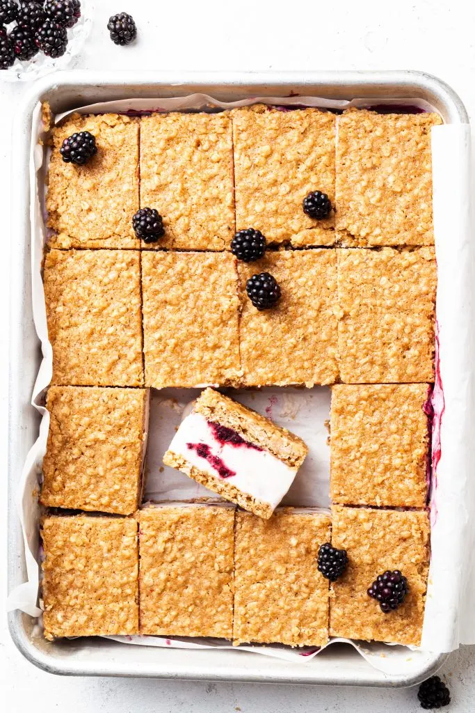 A rectangular metal pan filled with sliced ice cream bars - one is lying on its side revealing the vanilla ice cream and berry swirl. 