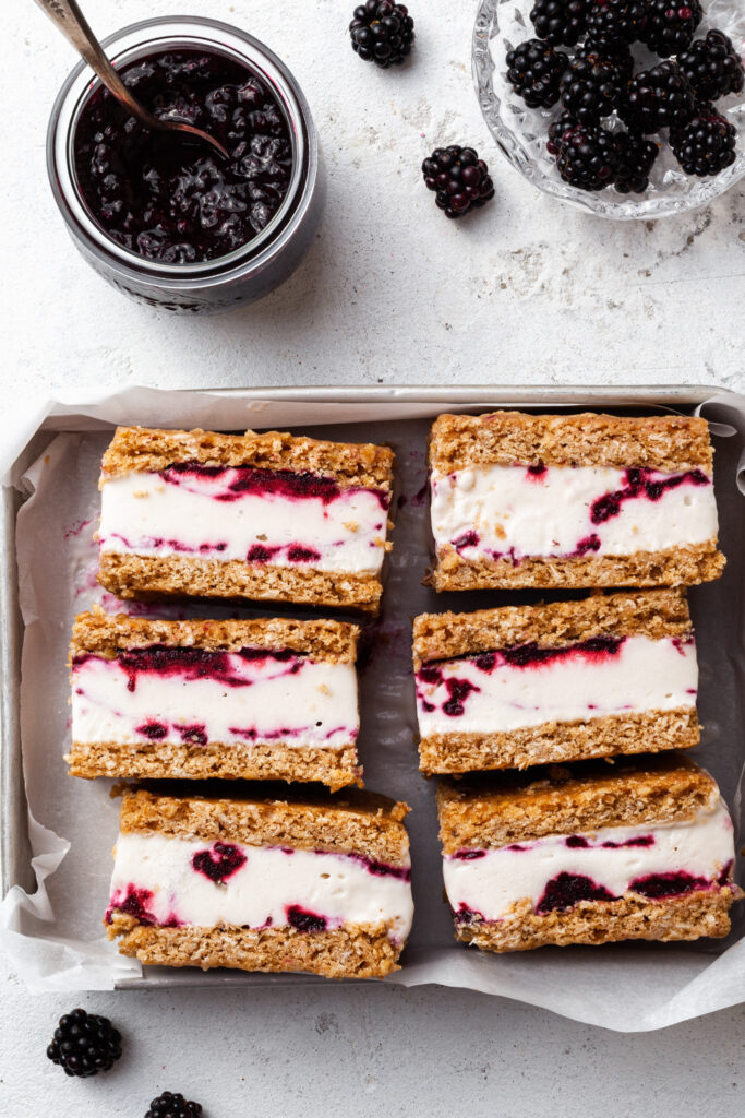 A small metal tray filled with 6 ice cream cookie bars, beside a jar of jam and a small glass dish of berries. 