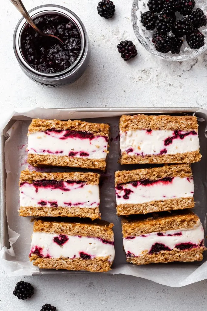 A small metal tray filled with 6 ice cream cookie bars, beside a jar of jam and a small glass dish of berries. 