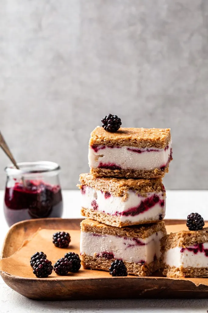 A tower of 3 ice cream cookie sandwiches on a wood tray lined with brown parchment paper.