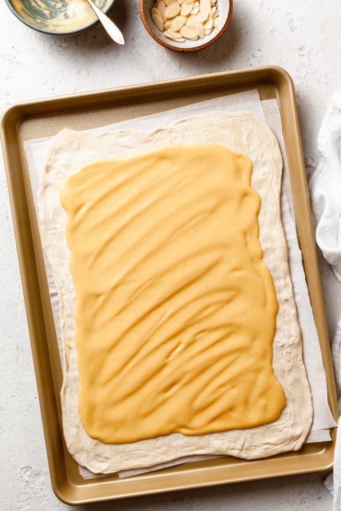 Pastry rolled out to a rectangle, spread with a yellow colored cream filling. 